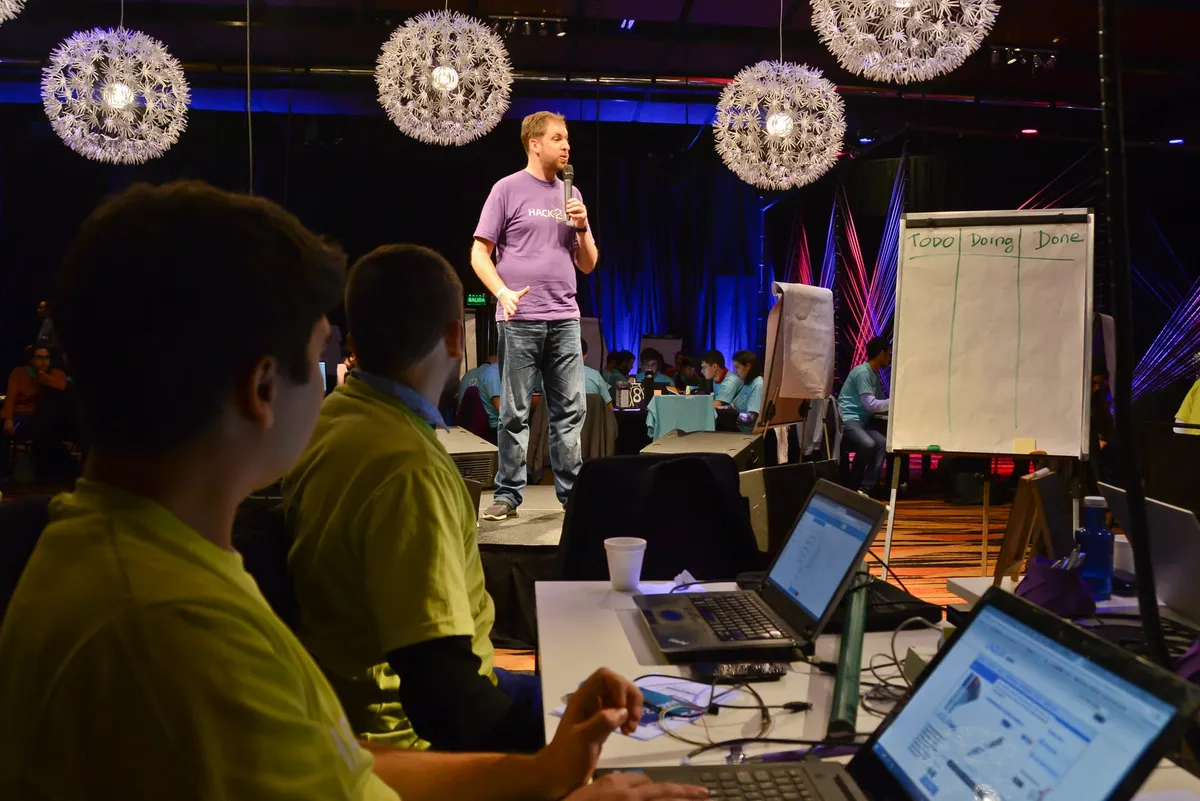Hack2In con equipos trabajando en laptops y facilitación en escenario
